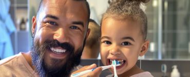 Pai escovando os dentes da filha com uma escova de dente infantil